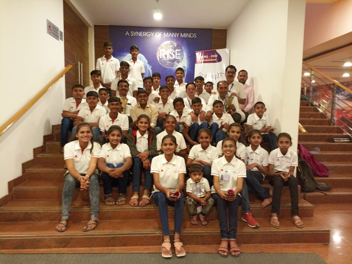 Students and instructors in corporate setting with 'Synergy of Many Minds' banner